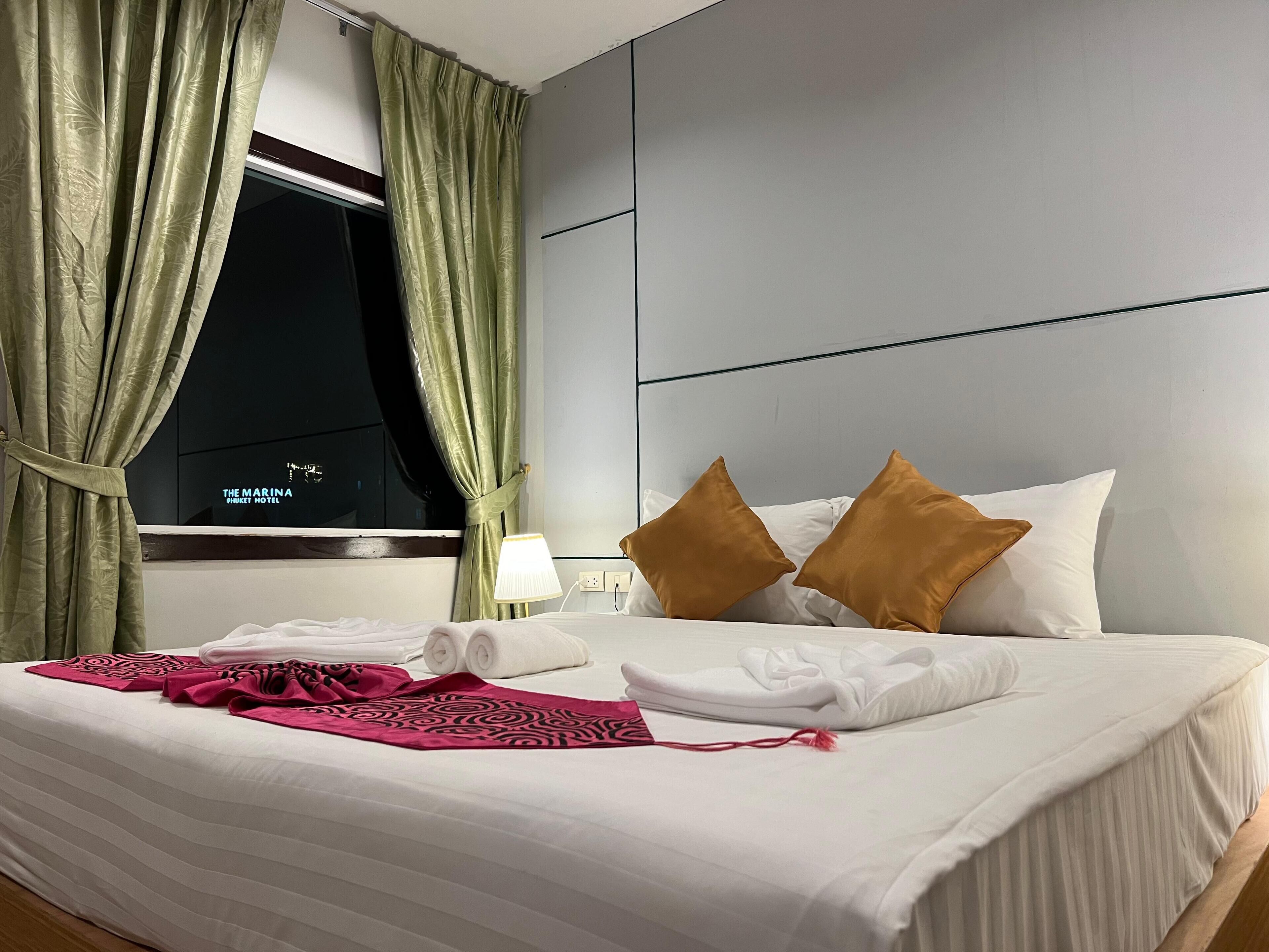 A hotel room with a neatly made bed, a window with curtains, and a view of the hotel name on the window.