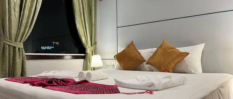 A hotel room with a neatly made bed, a window with curtains, and a view of the hotel name on the window.