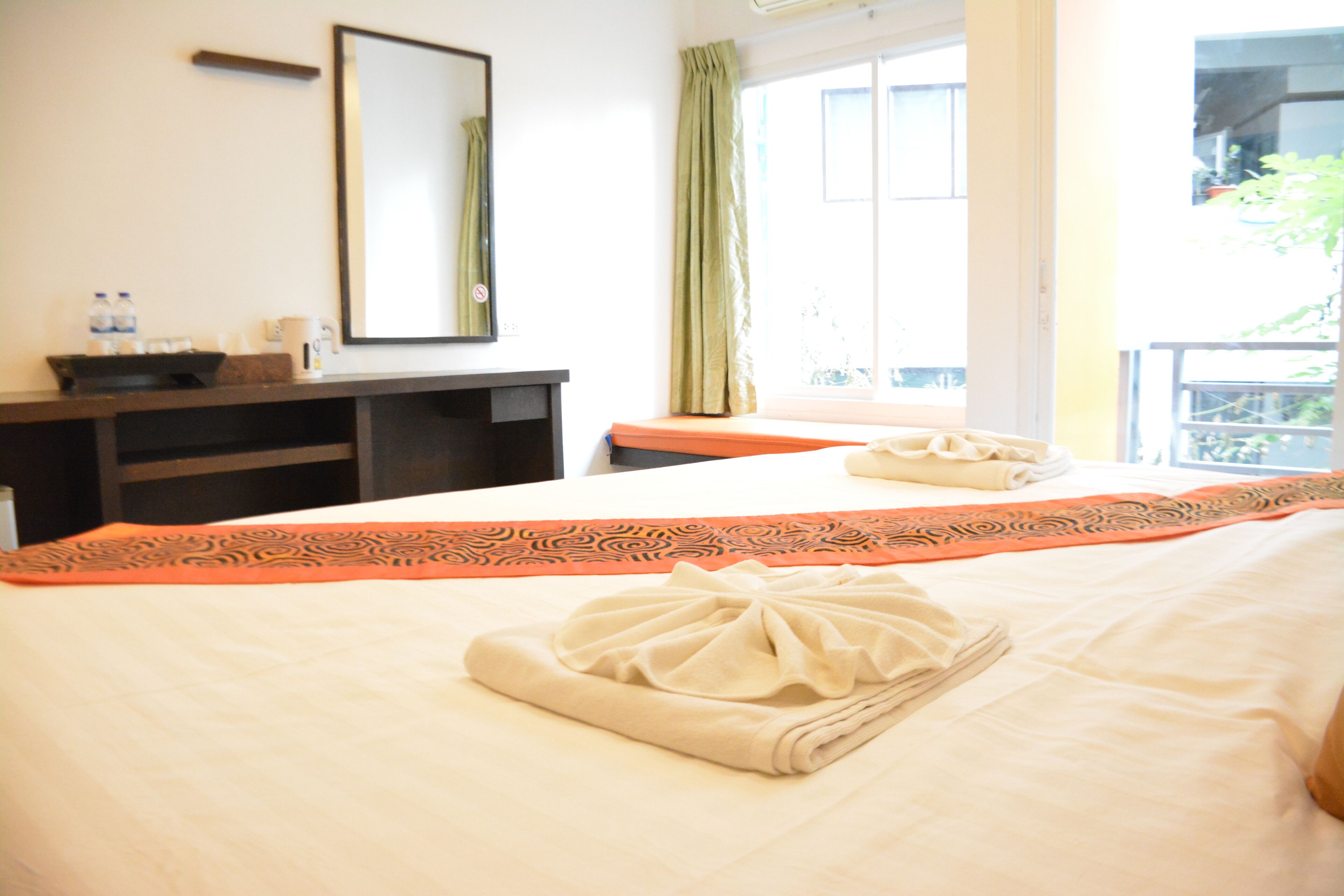 A hotel room with a bed, a desk, a mirror, and a window with curtains.