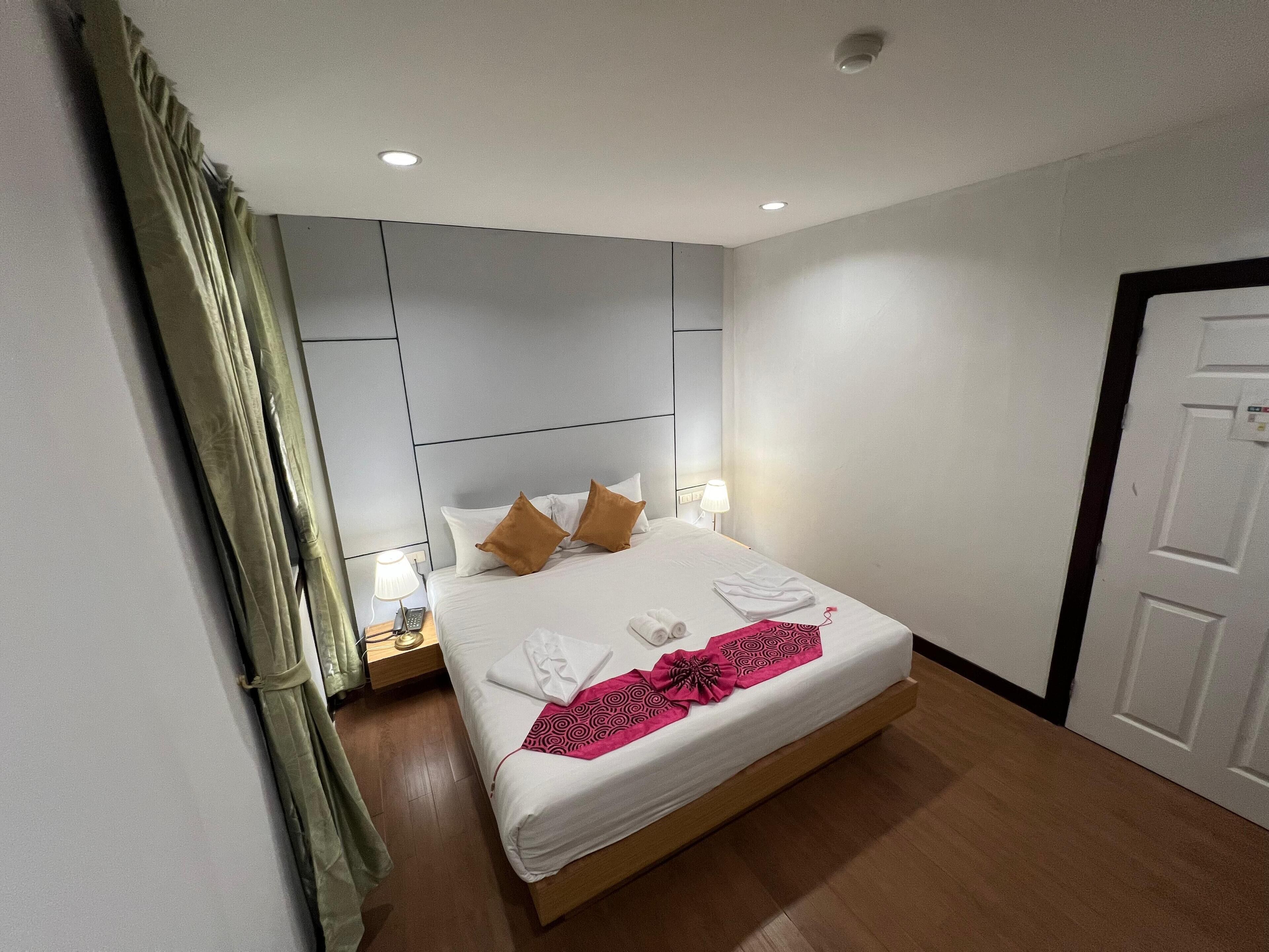 A hotel room with a bed, bedside tables, a nightstand, a door, and a curtain.