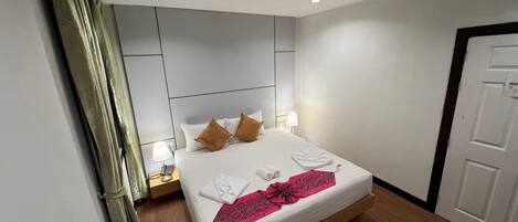 A hotel room with a bed, bedside tables, a nightstand, a door, and a curtain.