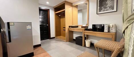 A compact kitchen with a refrigerator, wooden cabinets, a microwave, and a small table with a basket.
