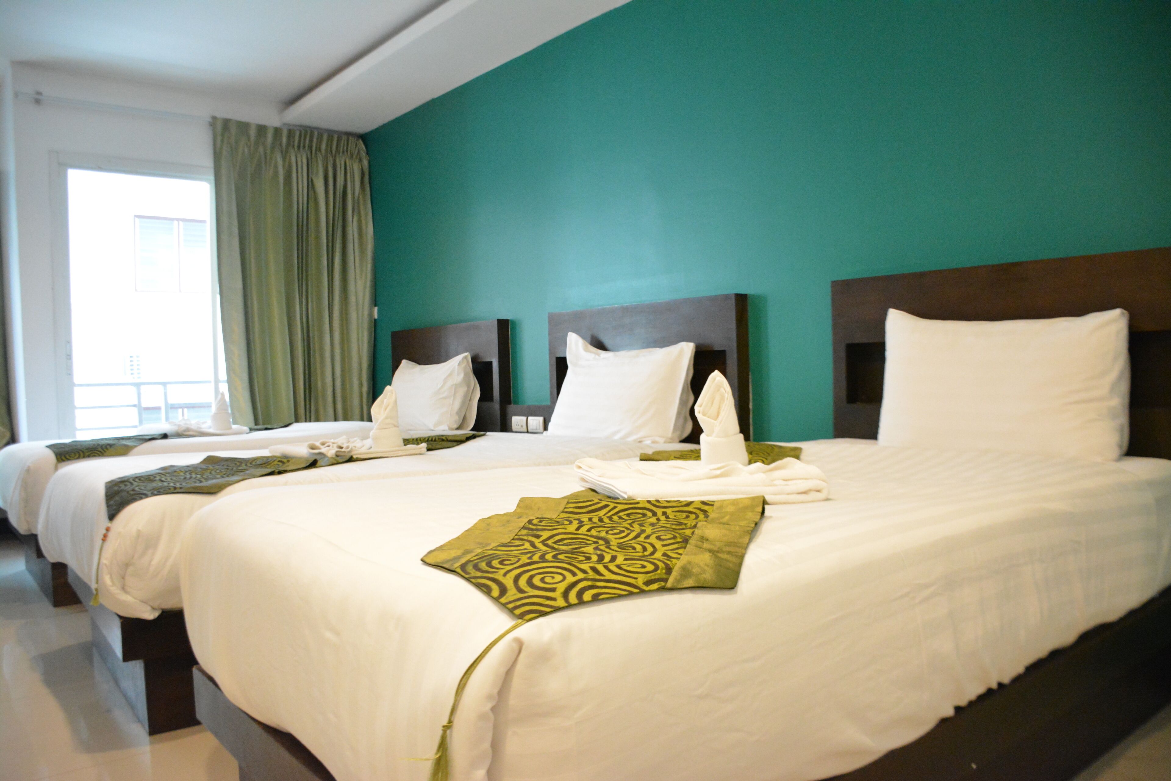 Una habitación de hotel con dos camas, paredes color verde azulado y un ventanal con cortinas.