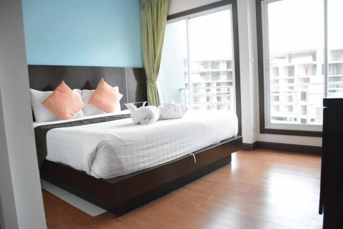 A modern hotel room with a bed, large windows, and a view of buildings.