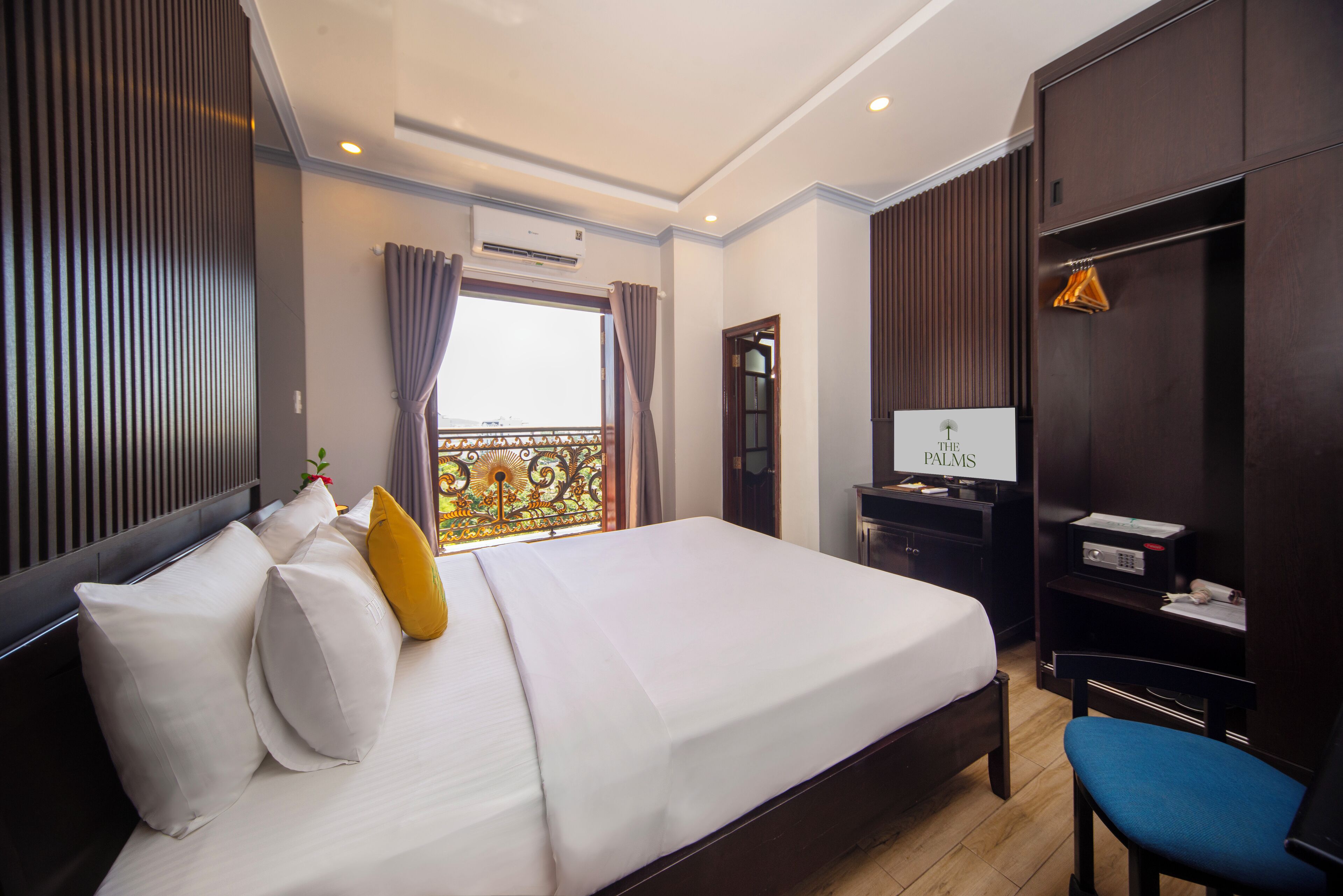 A hotel room with a large bed, a desk with a computer, a chair, and a wardrobe.