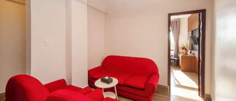 A modern living room with a red sofa, a small white side table, and a wooden floor.