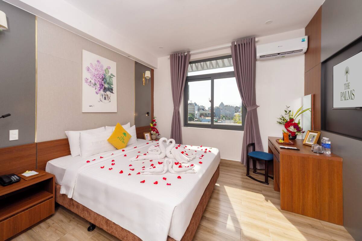 Une chambre d’hôtel avec un lit, un bureau, une chaise, une table de chevet et une fenêtre avec des rideaux.