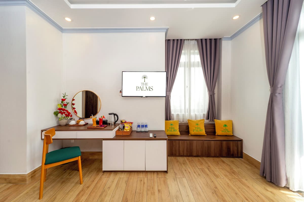Une pièce moderne avec un bureau en bois, une chaise verte, un banc avec des coussins jaunes, un téléviseur fixé au mur et une fenêtre avec des rideaux.