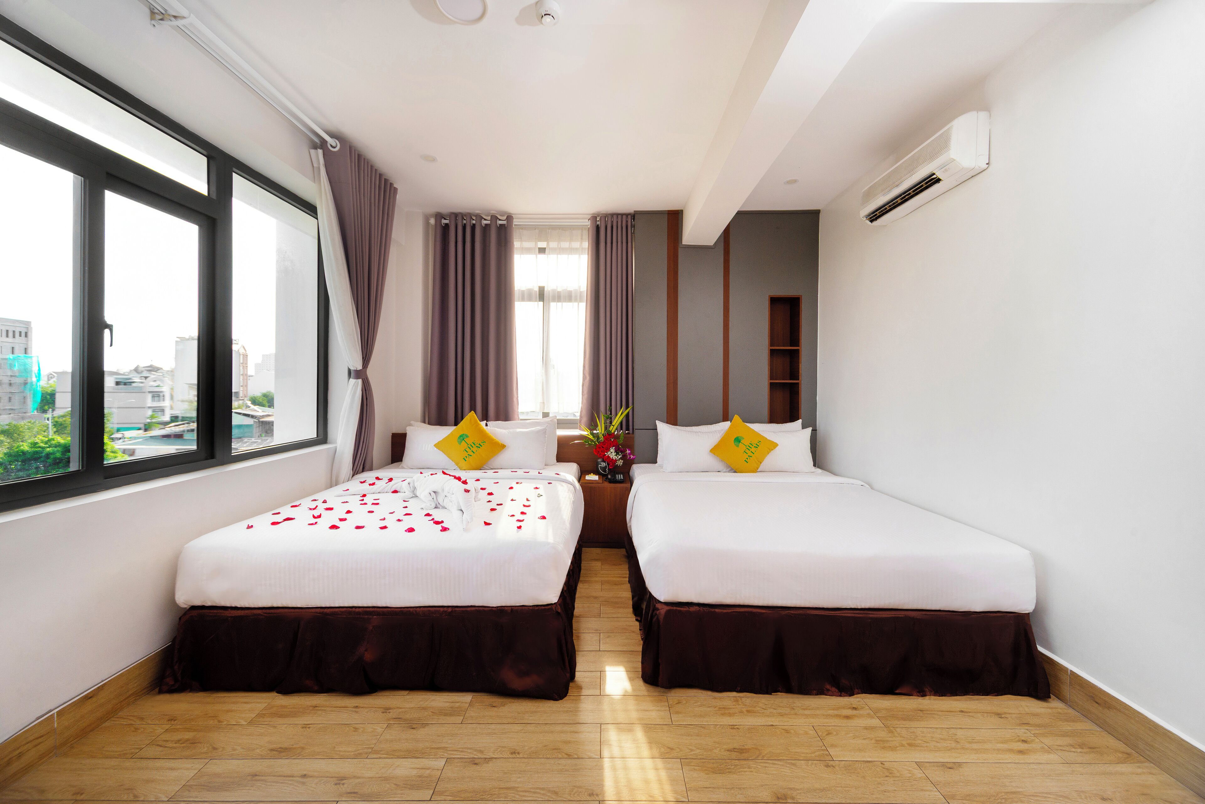 Habitación de hotel con dos camas, un ventanal grande y vistas a la ciudad.