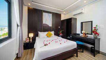 A hotel room with a large bed, a desk, a chair, a nightstand, a lamp, a mirror, and a view of the city.