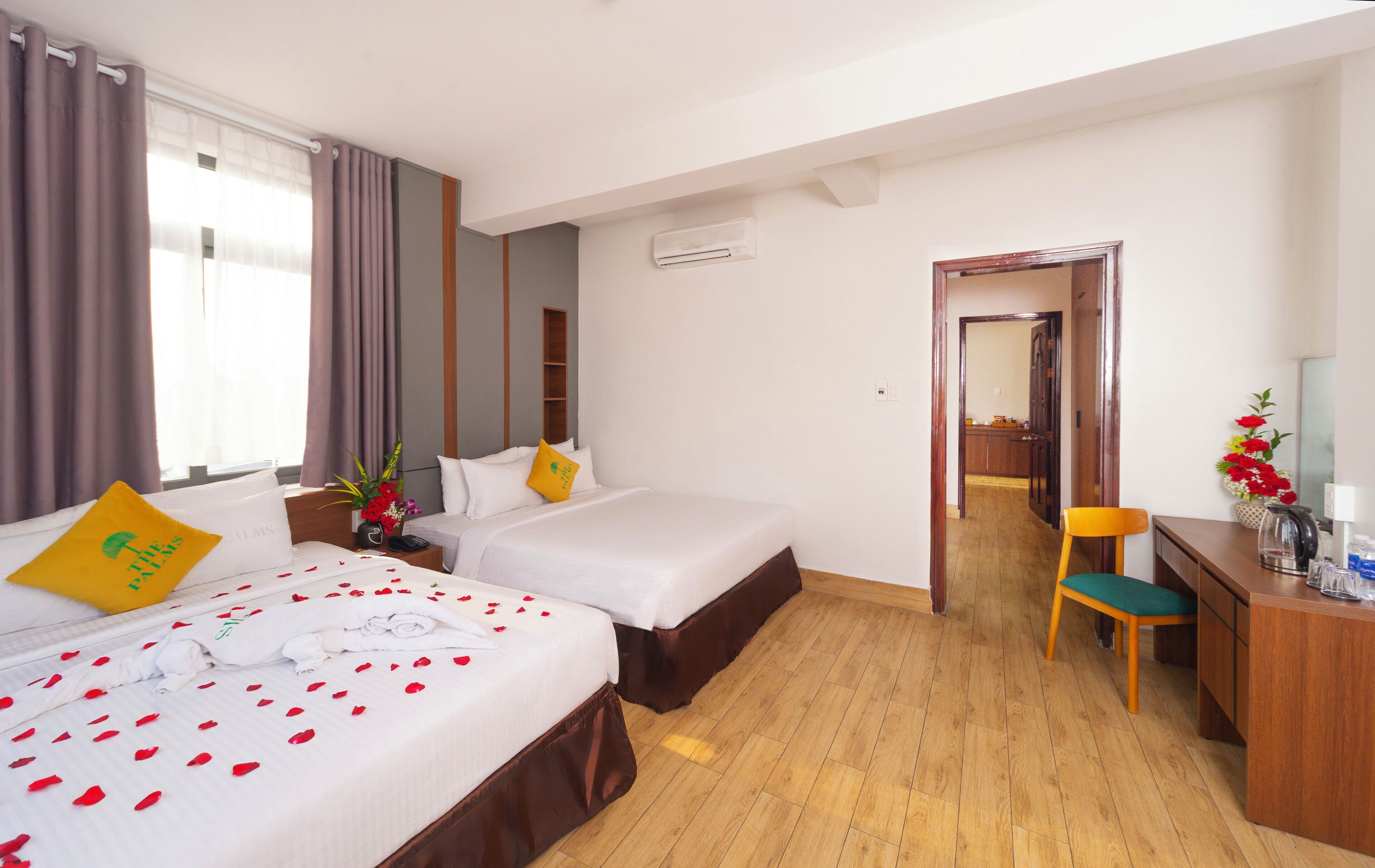A hotel room with two beds, a wooden desk, a chair, a mirror, and a view of the hallway.