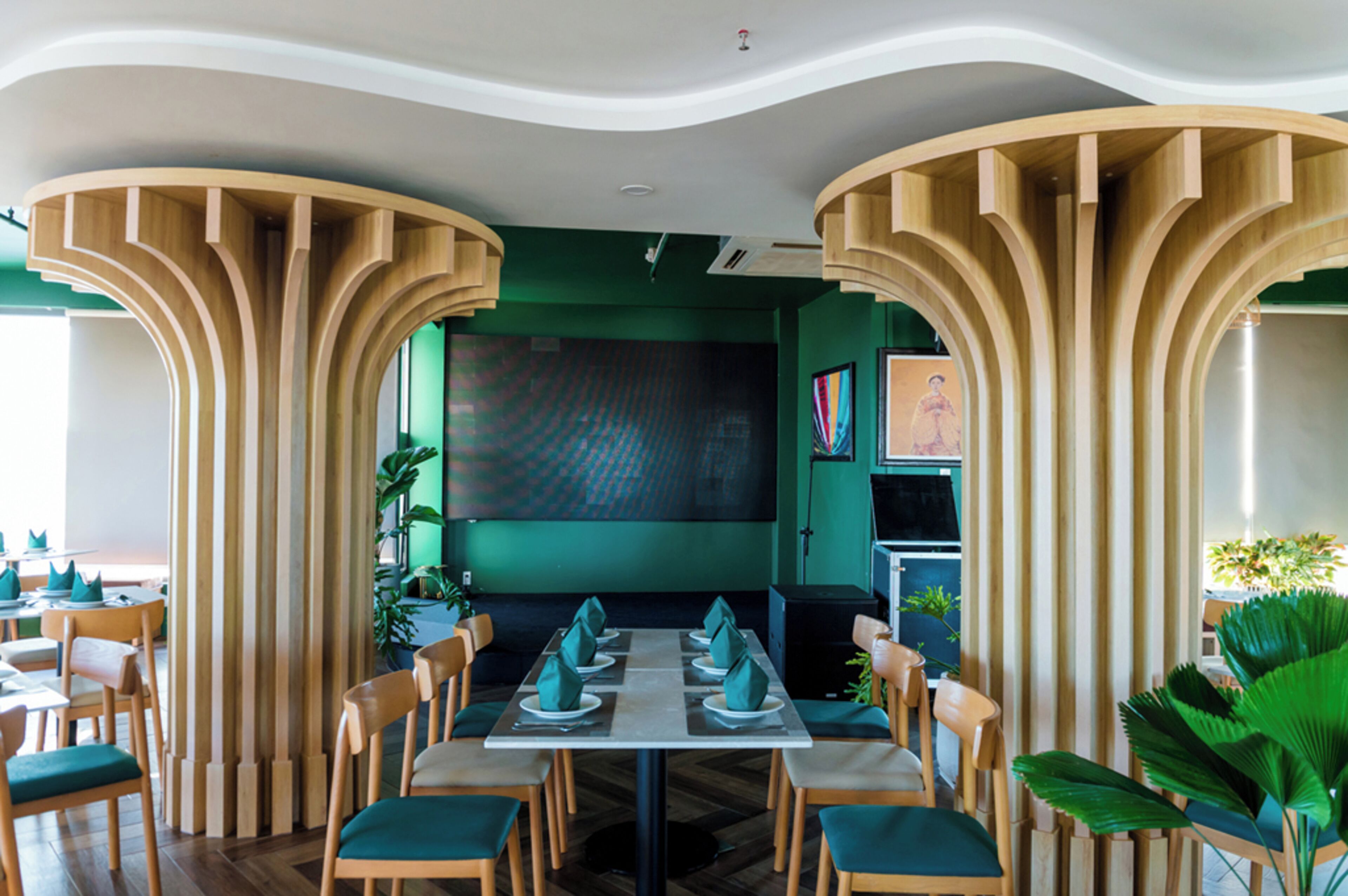 A restaurant with a modern design, featuring wooden pillars, green walls, and a central dining table with chairs.