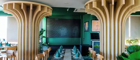 A restaurant with a modern design, featuring wooden pillars, green walls, and a central dining table with chairs.