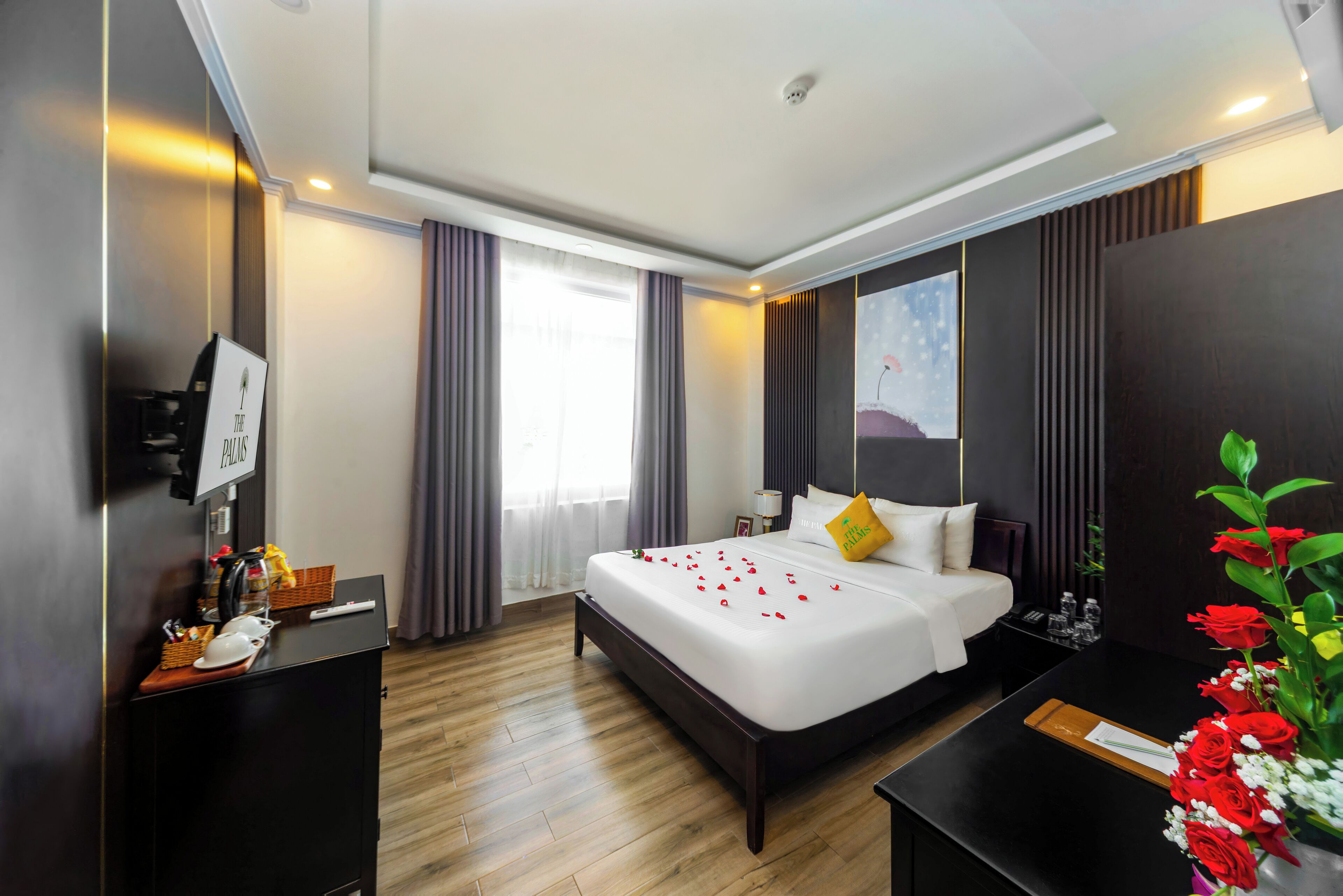A hotel room with a large bed, a desk, a TV, and a window with curtains.