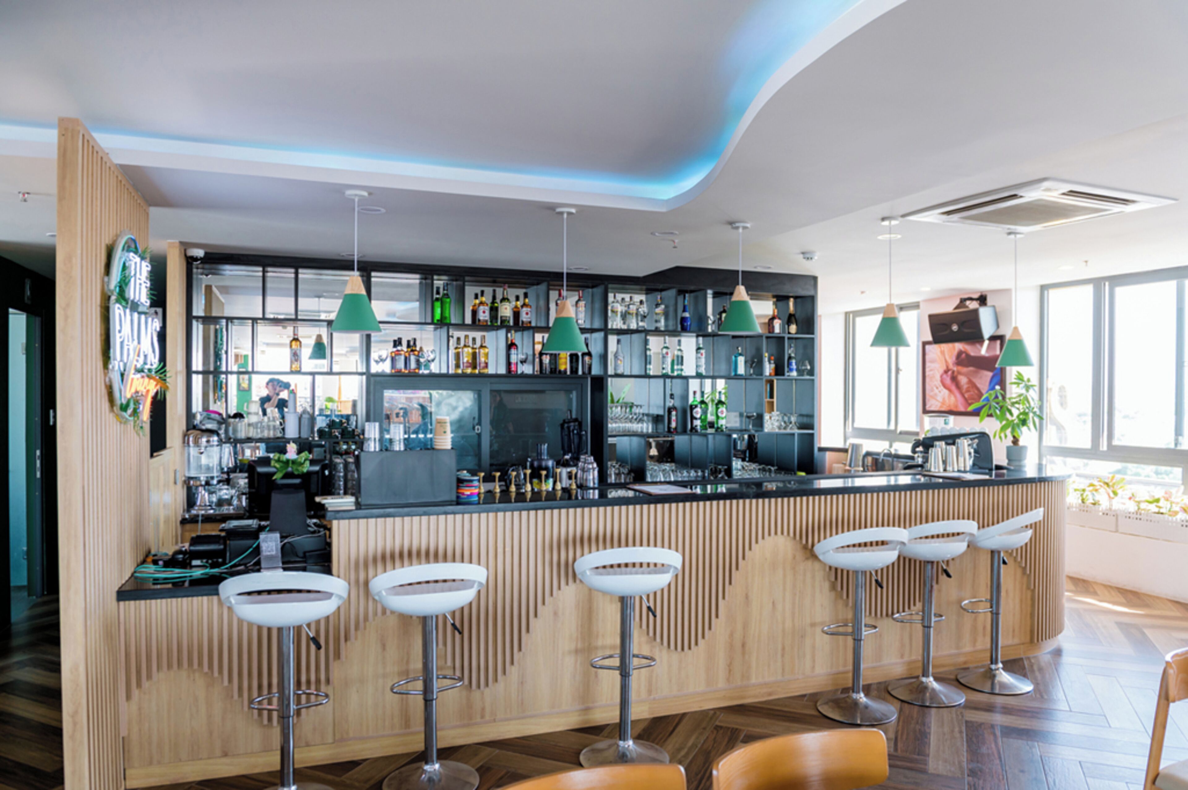 Un área de bar moderna con mostrador de madera, taburetes y lámparas colgantes.