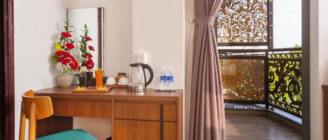 A wooden desk with a chair, a mirror, a floral arrangement, a coffee maker, and a bottle of water.