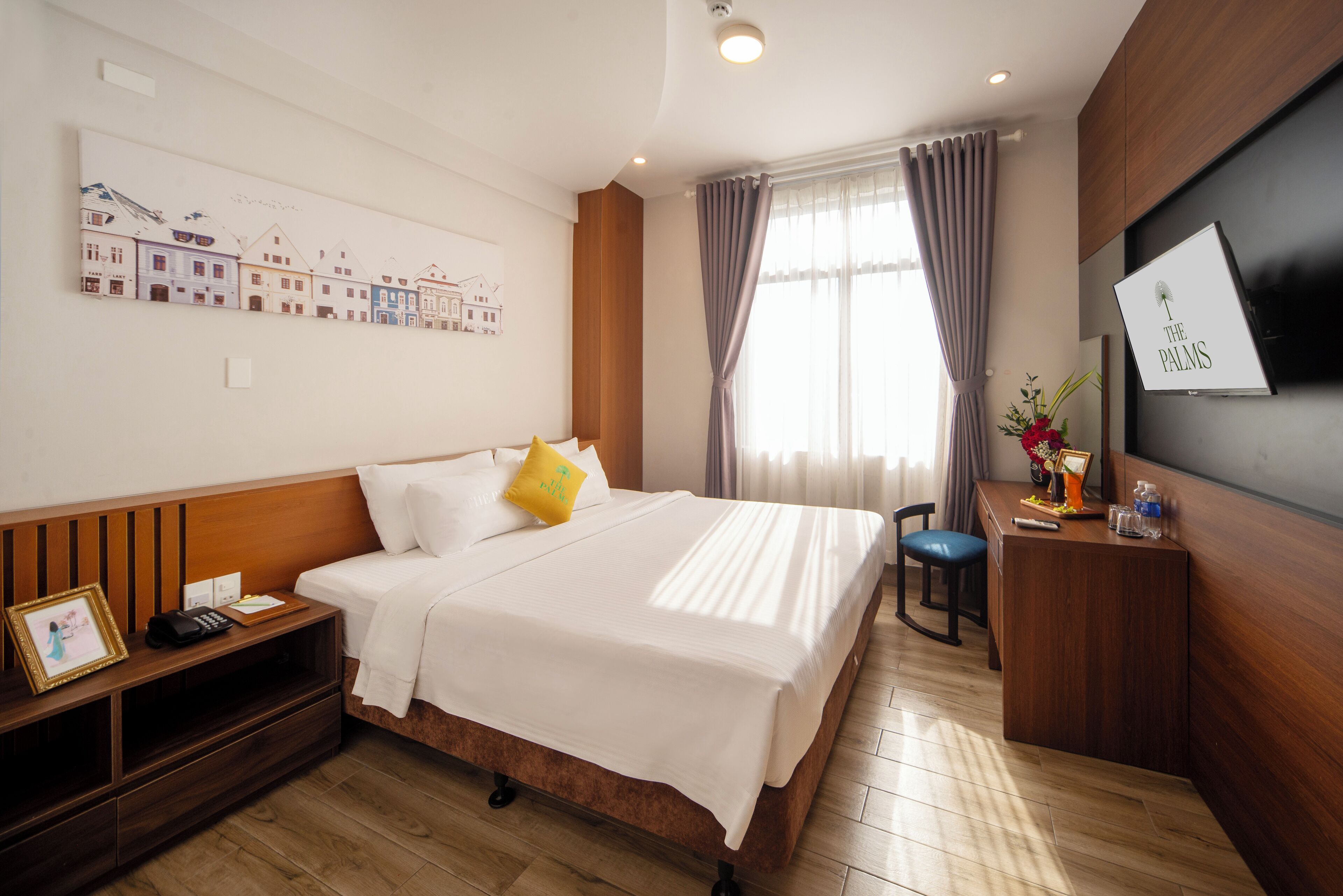 A hotel room with a bed, bedside table, desk, and a large window with curtains.