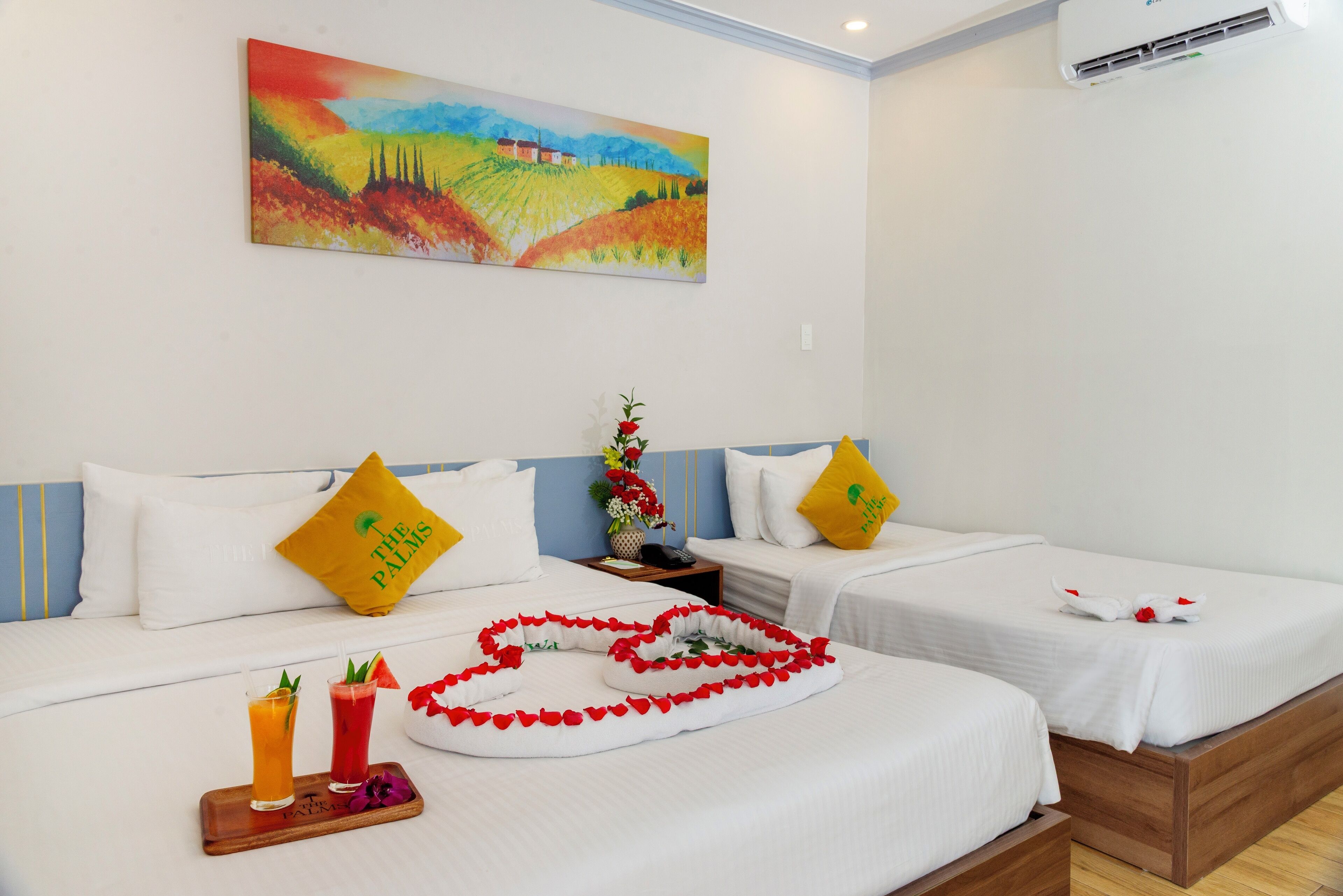 Camera d'albergo con due letti, un quadro appeso alla parete e un vassoio con bevande e fiori sul letto.