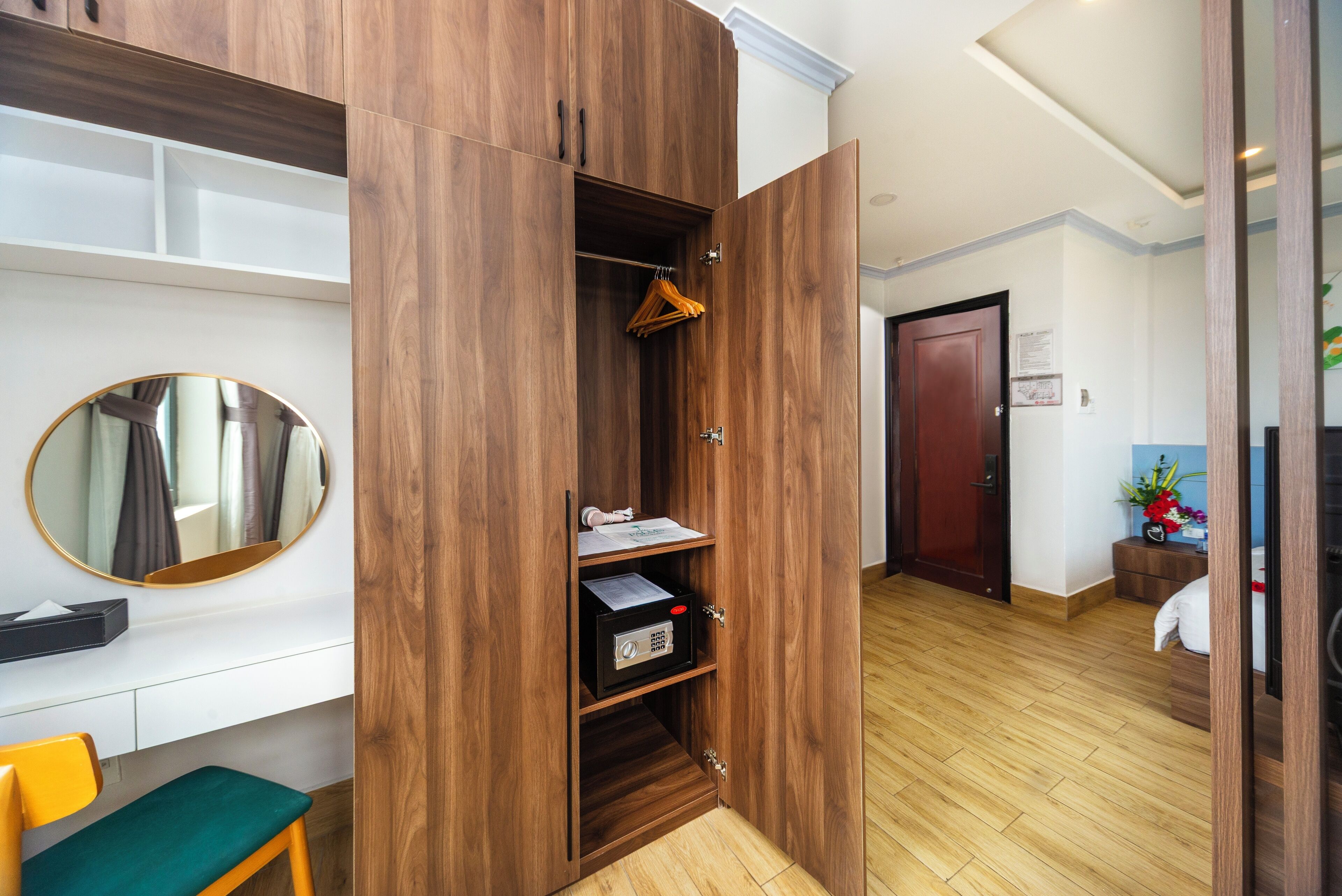 A room with a wooden wardrobe, a mirror, a desk, and a chair.