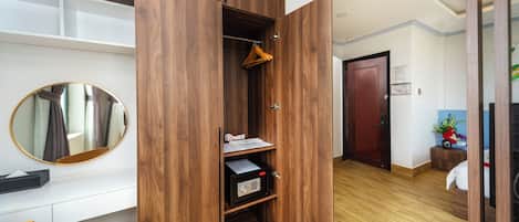 A room with a wooden wardrobe, a mirror, a desk, and a chair.