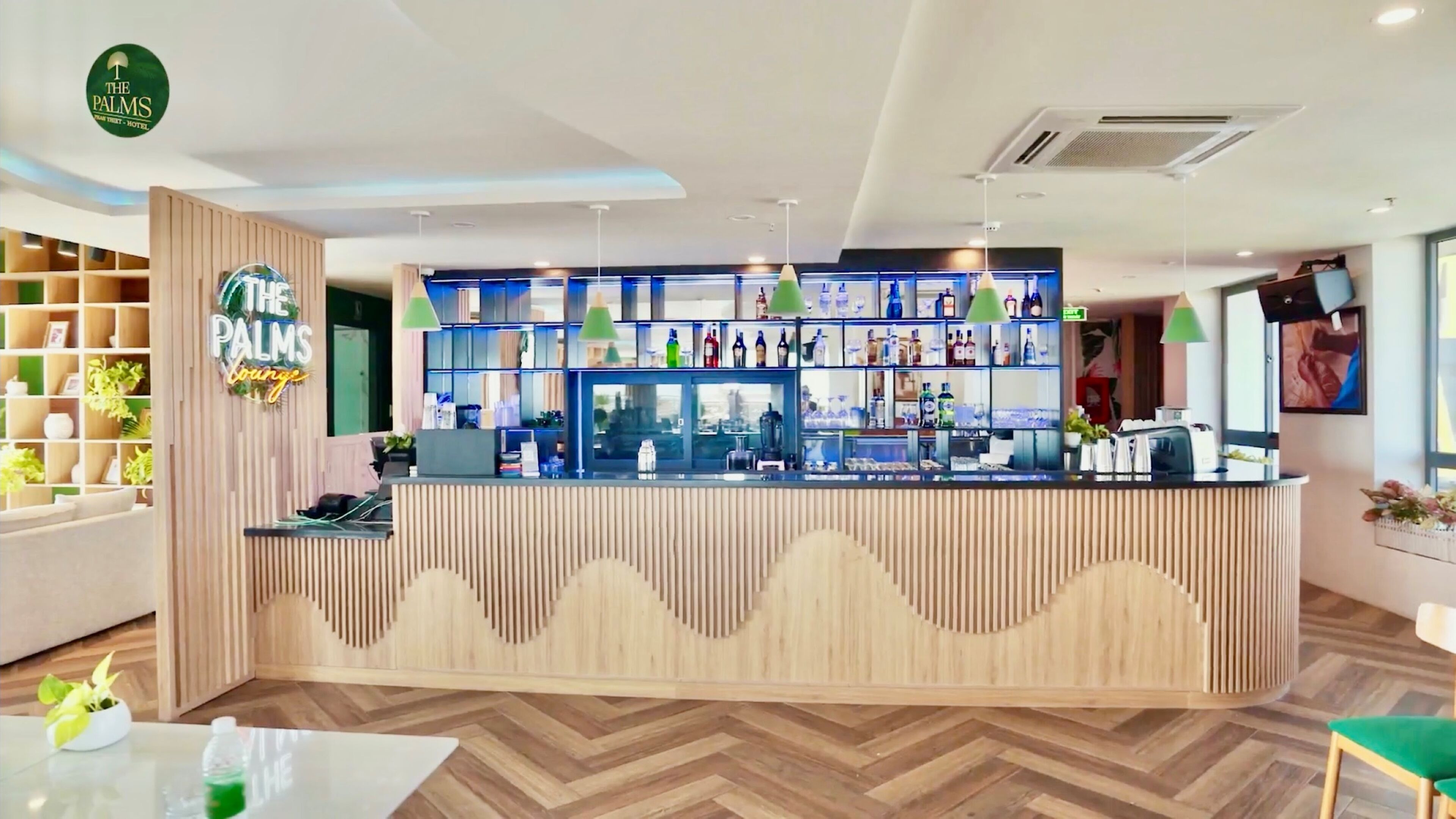 A reception area with a wooden reception desk, a bar area with shelves of bottles, and a seating area with a herringbone floor pattern.