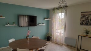 Ein Essbereich mit einem runden Tisch, Stühlen, einem an der Wand montierten Fernseher und Topfpflanzen.