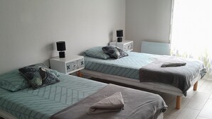 Ein Zimmer mit zwei Einzelbetten, jeweils mit Nachttisch und Lampe, einem kleinen Teppich und einem Fenster mit gemusterten Vorhängen.