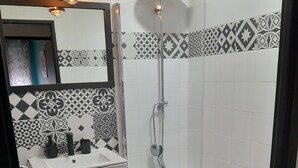 Ein modernes Badezimmer mit einem weißen Waschbecken, Fliesen in Schwarz-Weiß-Muster, einer Dusche und einer kleinen Holzablage mit einer Flasche.