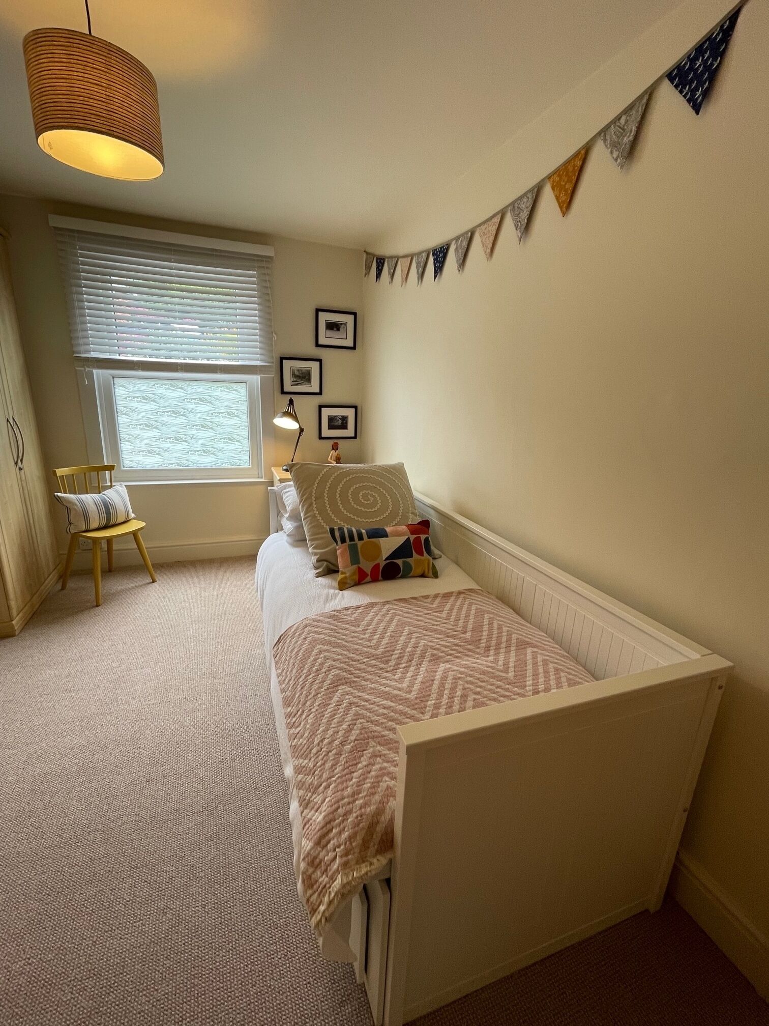 Un dormitorio acogedor con una cama individual, una ventana con persianas, una pequeña silla y una lámpara de pared.