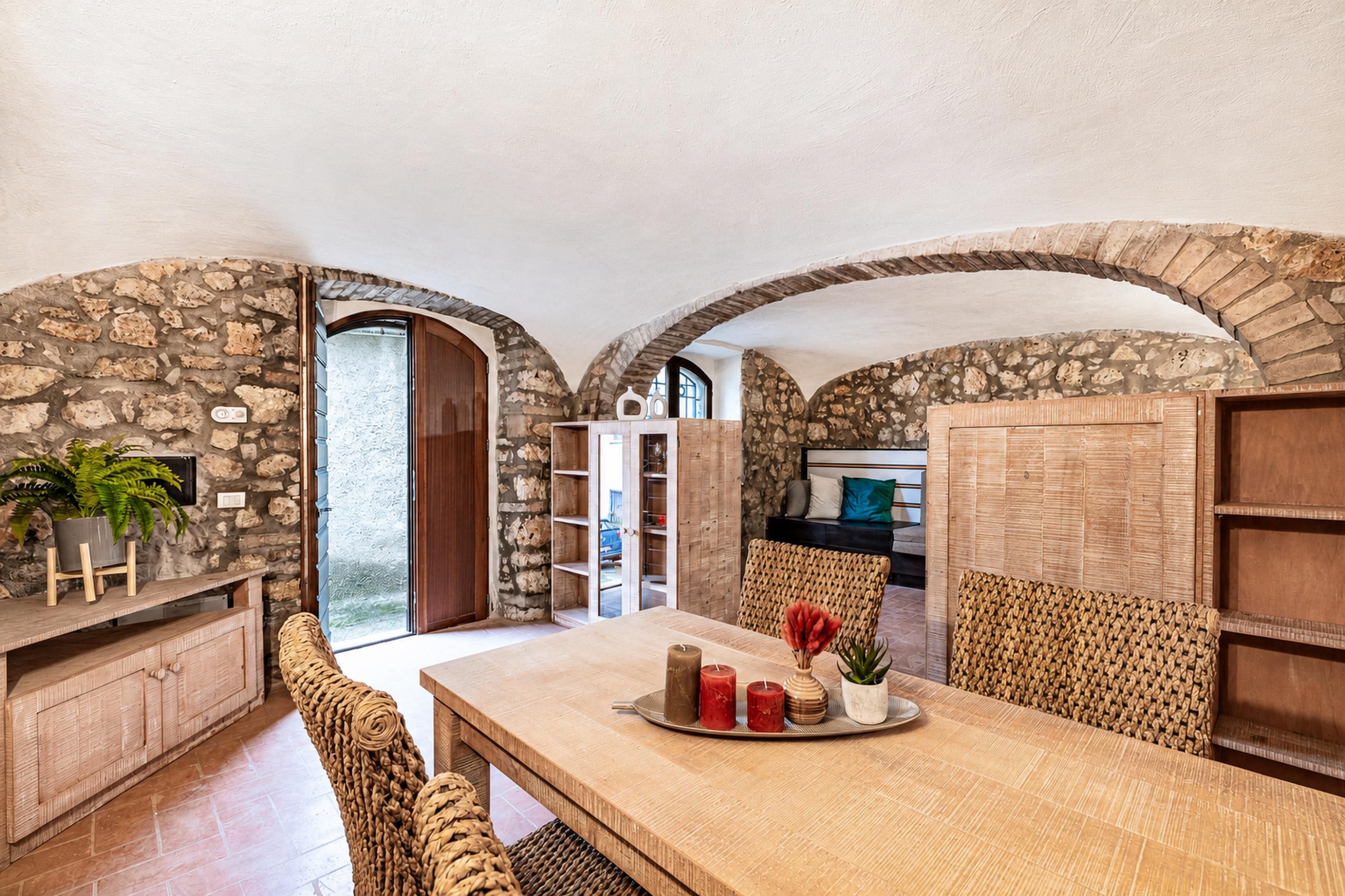 A dining area with a stone wall, wooden furniture, and a view through an archway.