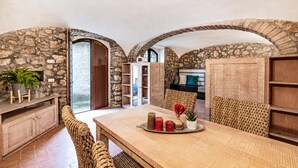 A dining area with a stone wall, wooden furniture, and a view through an archway.