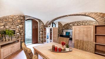 A dining area with a stone wall, wooden furniture, and a view through an archway.