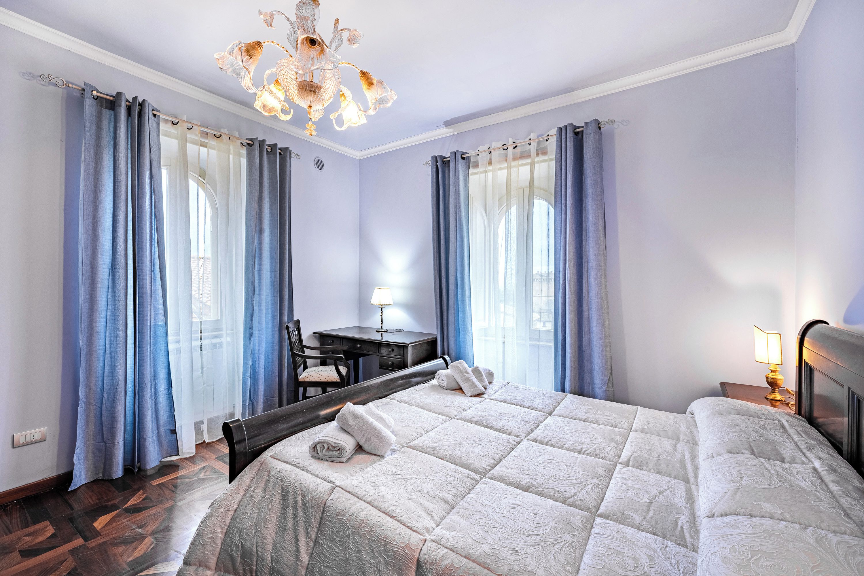 A hotel room with a bed, a desk, a chair, and a chandelier.