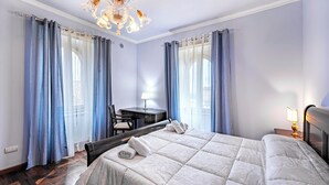 A hotel room with a bed, a desk, a chair, and a chandelier.
