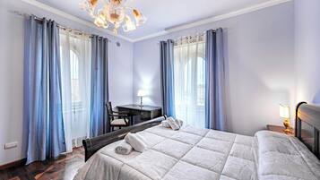 A hotel room with a bed, a desk, a chair, and a chandelier.