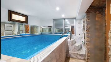 A swimming pool with a marble border, a stone wall, and a television mounted above the pool.