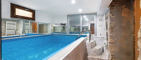 Uma piscina com borda de mármore, parede de pedra e televisão fixada acima da piscina.