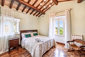 Une chambre à coucher avec un lit en bois, une table de chevet, un fauteuil à bascule et une vue sur la verdure par la fenêtre.
