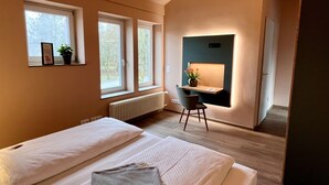 Een hotelkamer met twee bedden, een bureau, een stoel en een raam met uitzicht op bomen.