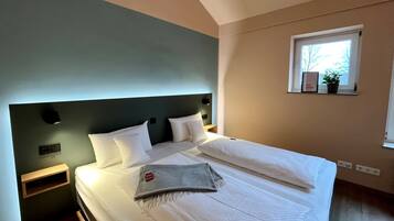 Een moderne slaapkamer met een groot bed, een hoofdbord, nachtkastjes, een raam met uitzicht en een klein plankje met een plantje.