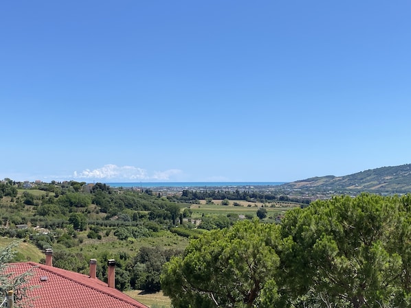 A rural landscape with a red-roofed building, green trees, and a distant view of the sea.