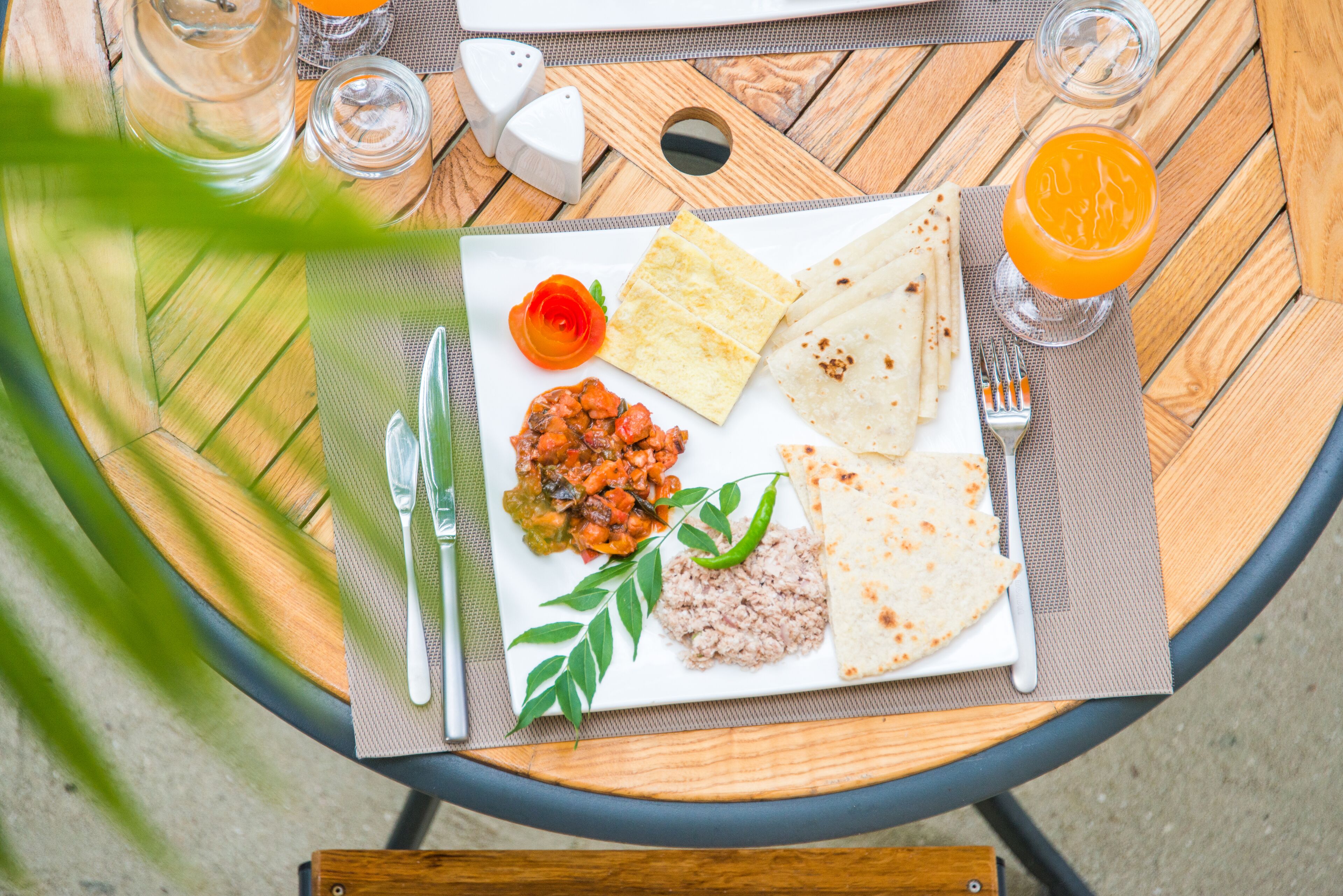 Comida sobre una mesa de madera, con un plato de alimentos, cubiertos y un vaso de jugo de naranja.