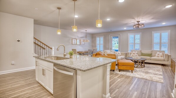 A spacious living area with a kitchen island, a dining table, and a seating area with sofas and ottomans.