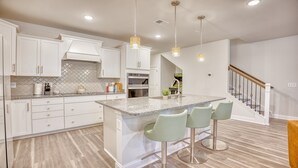A modern kitchen with white cabinetry, granite countertops, and a central island with bar stools. - 5128 Townes at Barefoot (North Myrtle Beach)