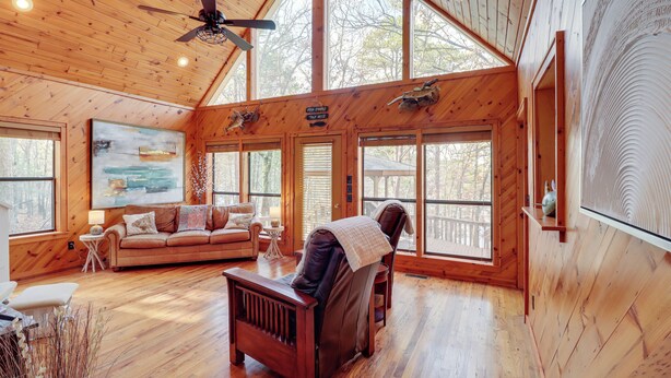 Eine geräumige Holzhütte mit hohen Decken, Holzwänden und großen Fenstern. Ein gemütlicher Sitzbereich mit einer Couch und einem Sessel lädt zum Entspannen ein.