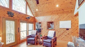 Ein gemütliches Blockhaus-Interieur mit Holzwänden und -böden, zwei Ledersesseln, einem kleinen Tisch und einem Kamin.