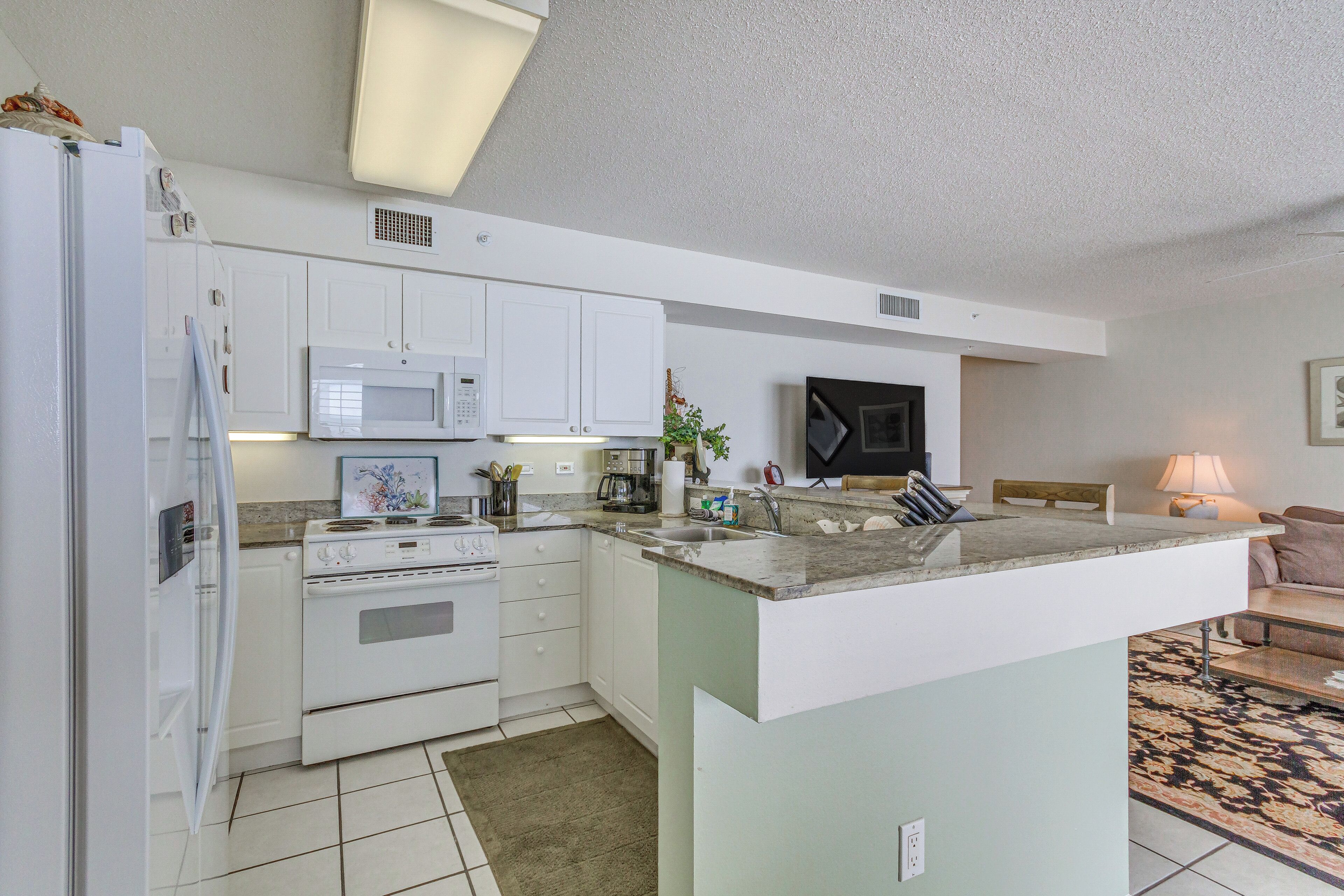 A modern kitchen with white cabinets, a microwave, a stove, and a sink.