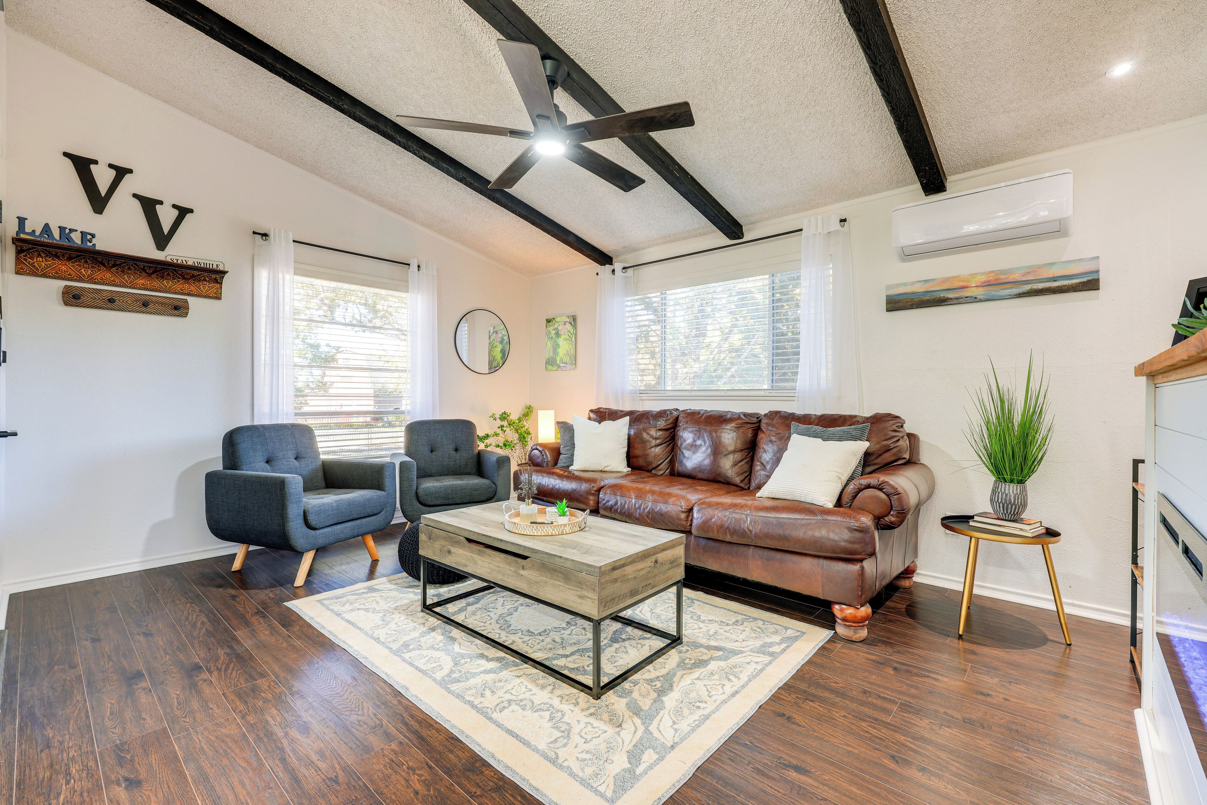 A living room with a dark wood floor, a brown leather sofa, a blue armchair, a wooden coffee table, and a ceiling fan.
