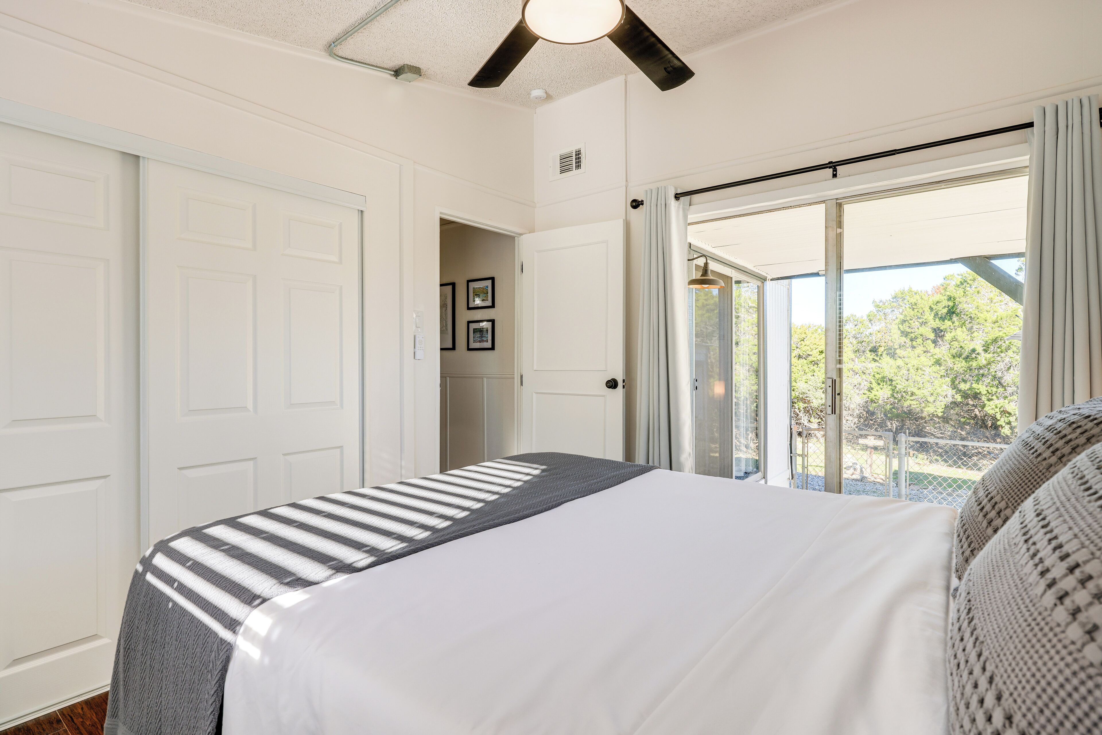 A bedroom with a bed, a ceiling fan, and a view of the outdoors through a sliding door.