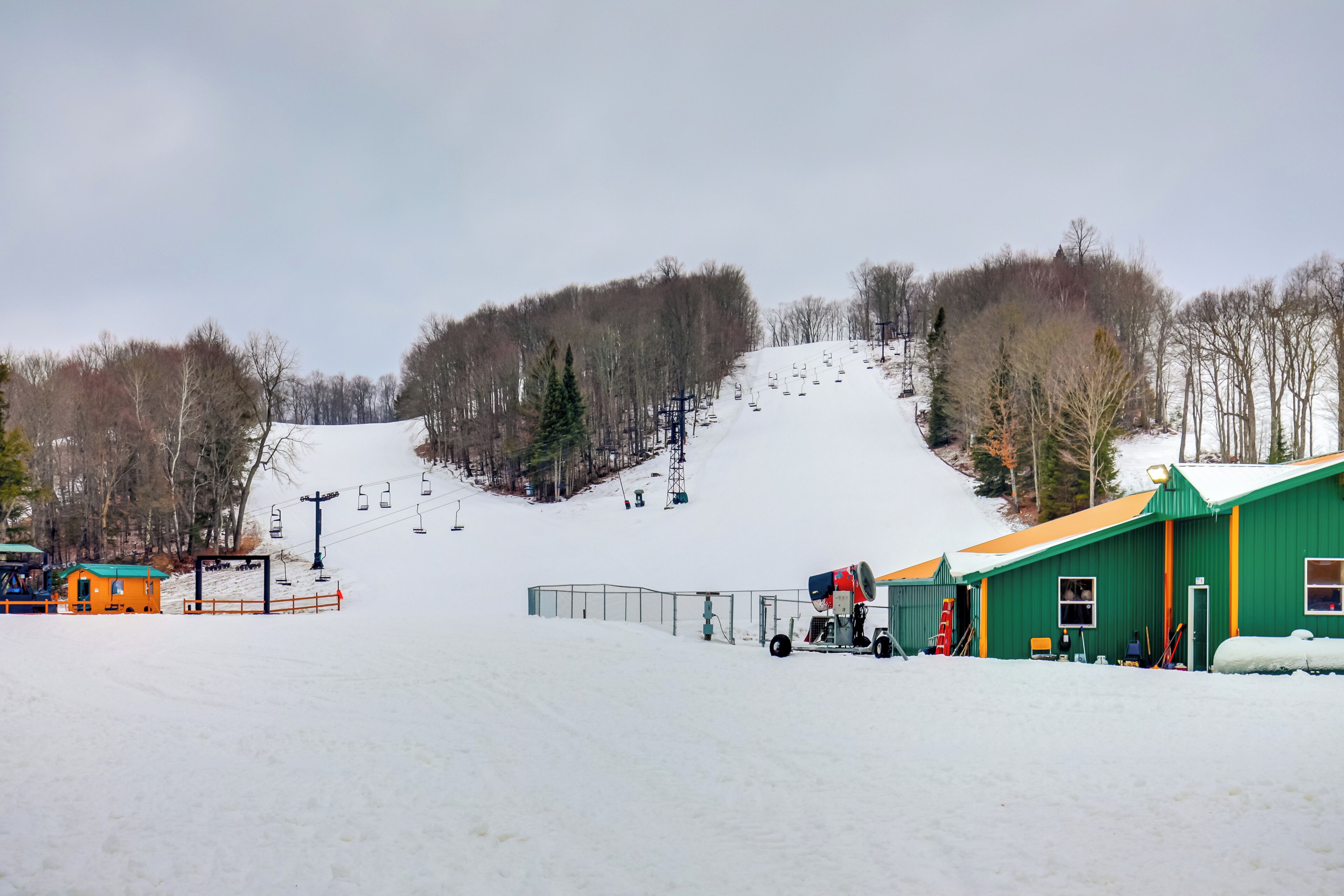 A ski resort with a green building, a ski lift, and a snow-covered slope.